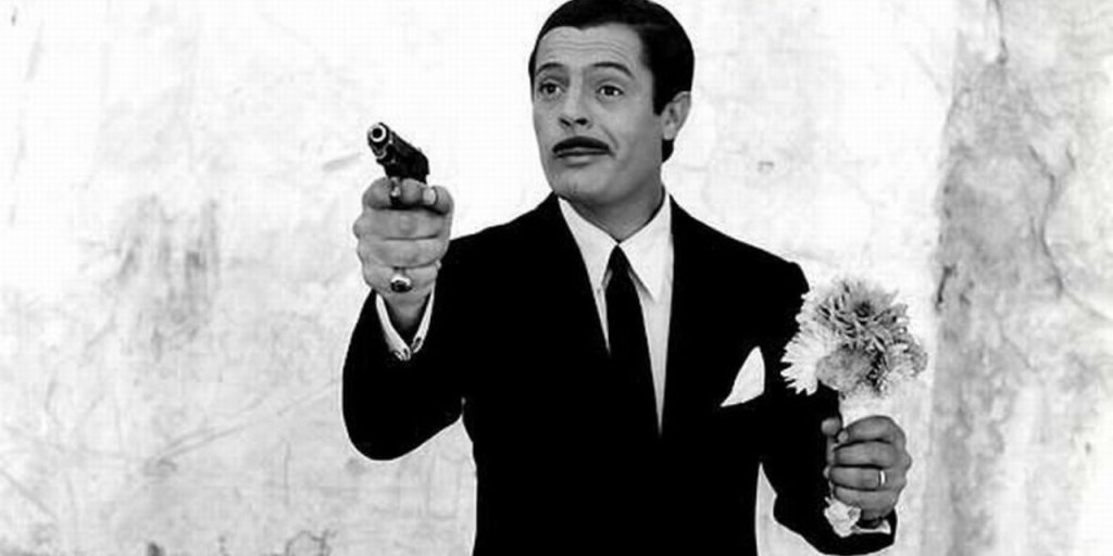 Marcello Mastroianni with a gun in one hand and a flower in the other